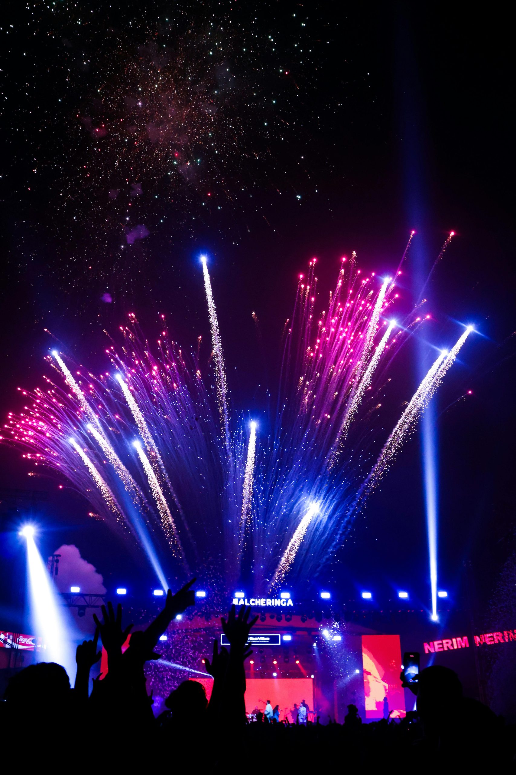 Vibrant fireworks illuminate the night sky at a lively concert in India.